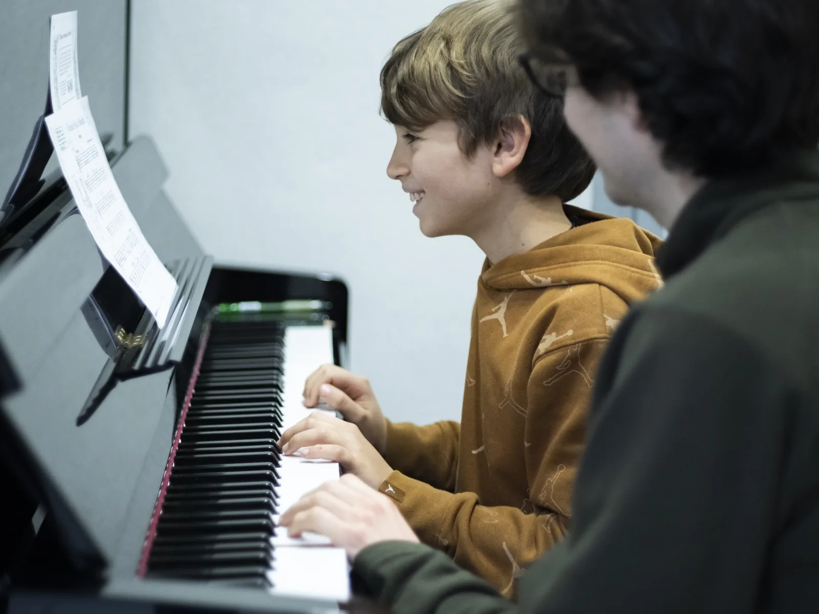 Un allievo sorride mentre suona il pianoforte durante una lezione, affiancato dal docente